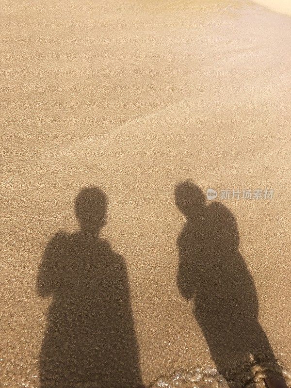 强烈阳光下金色沙滩的阴影，人们站在阳光下的轮廓/剪影